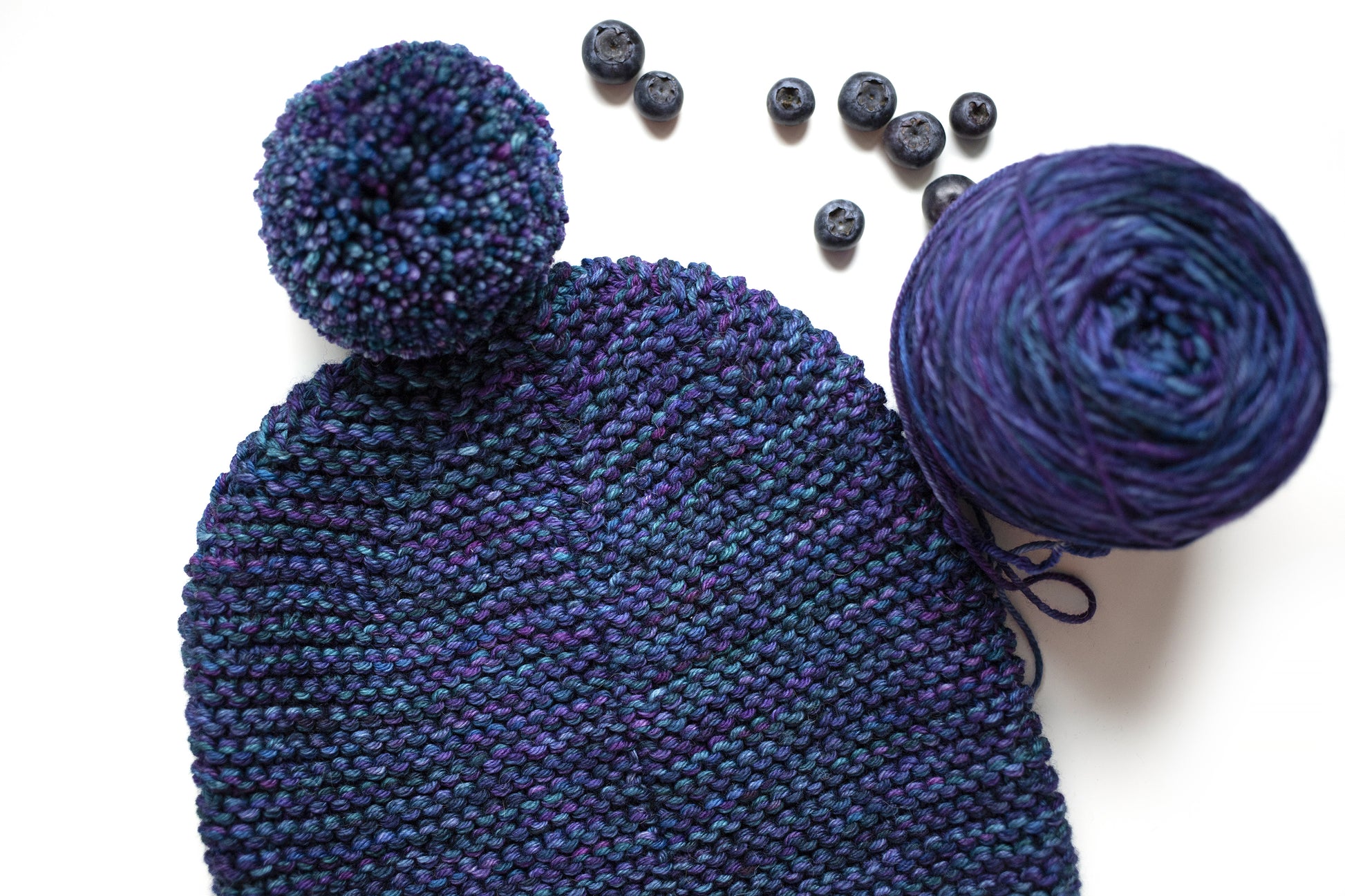 Back side of a blue and purple gradient wool garter stitch hand-knitted pom pom hat