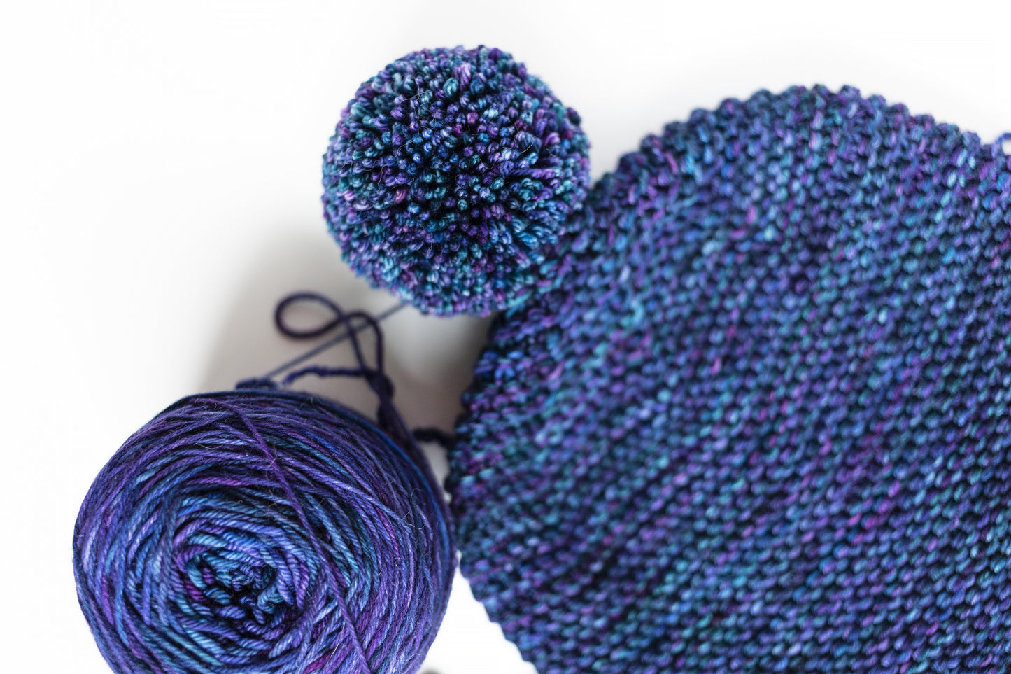 details of a blue and purple gradient wool garter stitch hand-knitted pom pom hat