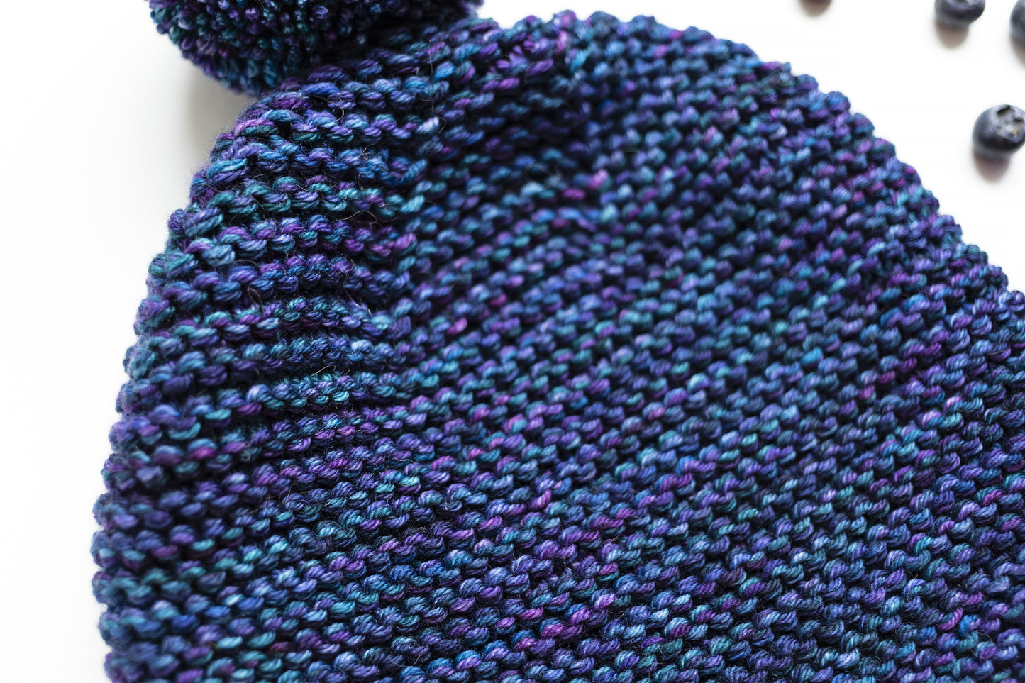 Texture of a blue and purple gradient wool garter stitch hand-knitted pom pom hat