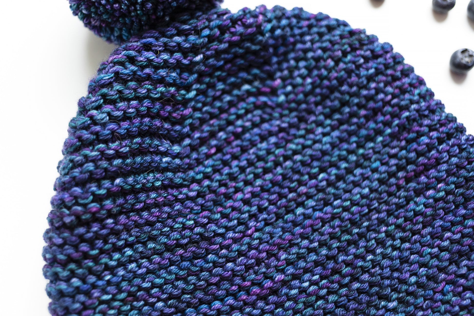 Texture of a blue and purple gradient wool garter stitch hand-knitted pom pom hat