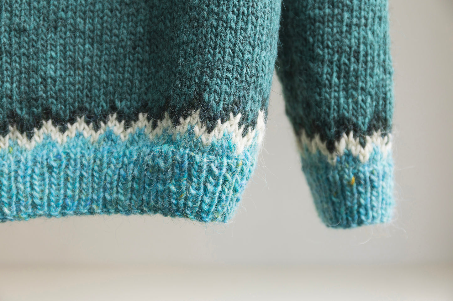 Cuff and hem details of a turquoise, white and black hand-knitted lopapeysa sweater in Puffins design