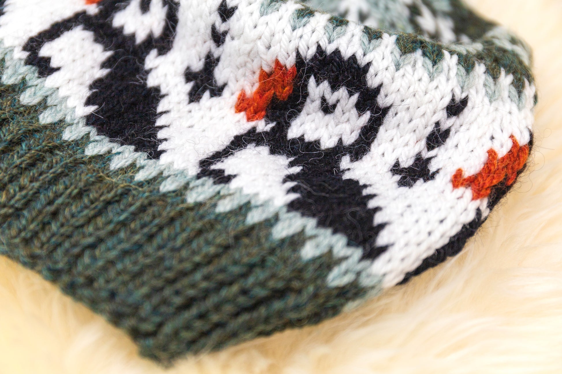 detail of a hand-knitted wool hat with a geometric pattern featuring puffins in green, black and white colors on a white background.