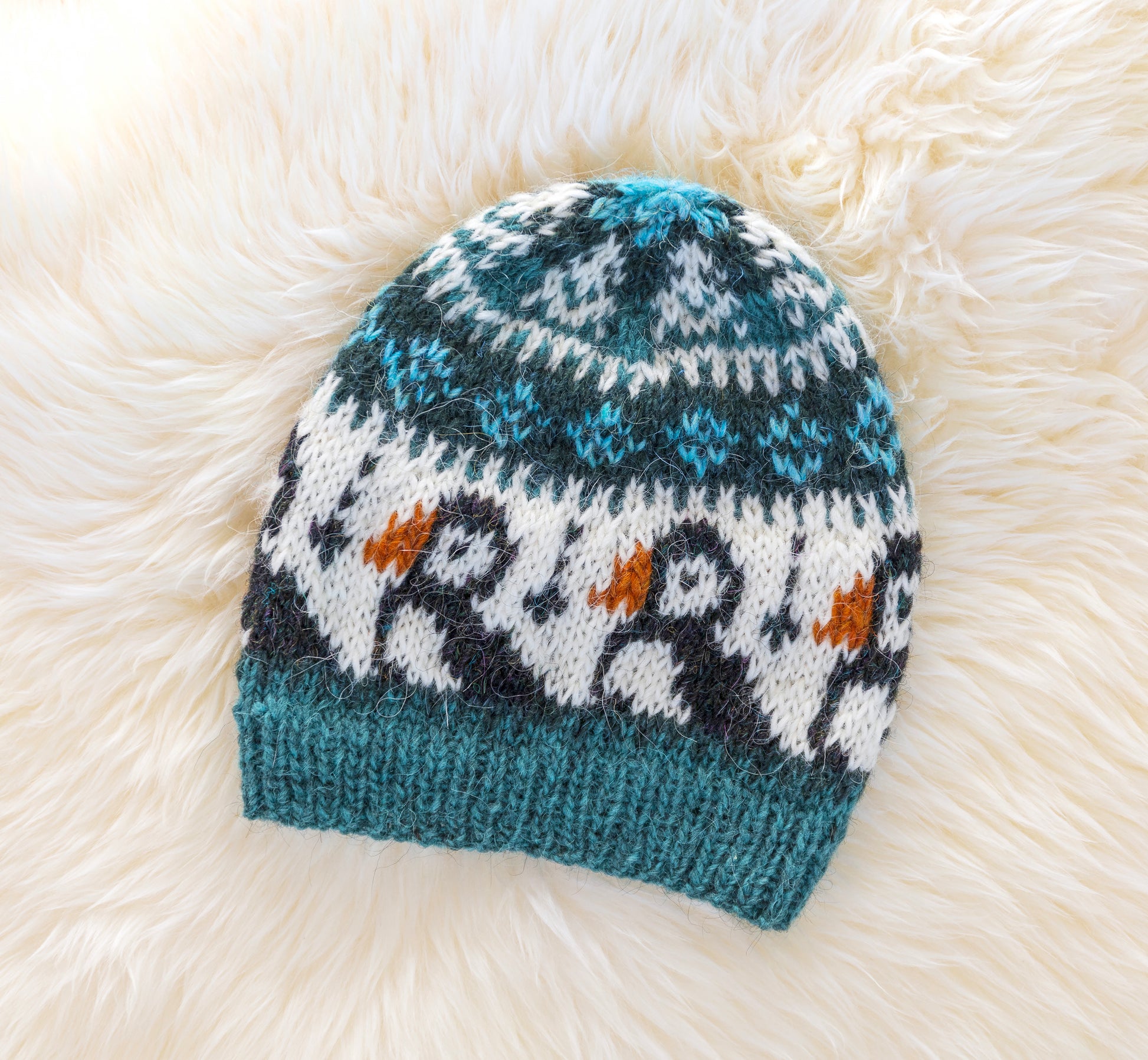 A hand-knitted wool hat with a geometric pattern featuring puffins in blue, black, and brown colors on a white background.