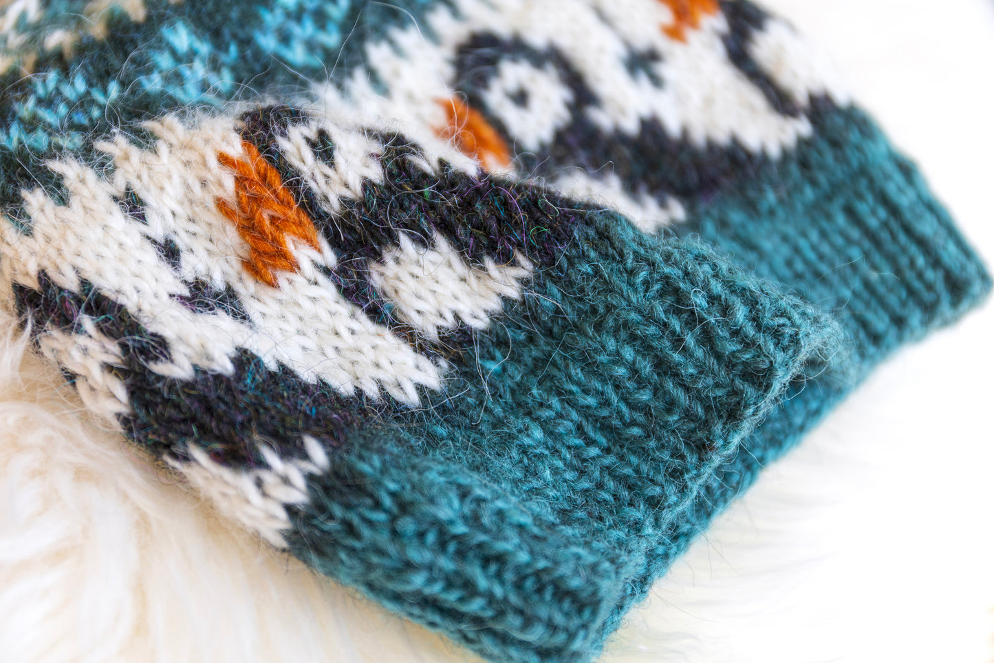 detail of a hand-knitted wool hat with a geometric pattern featuring puffins in blue, black, and brown colors on a white background.