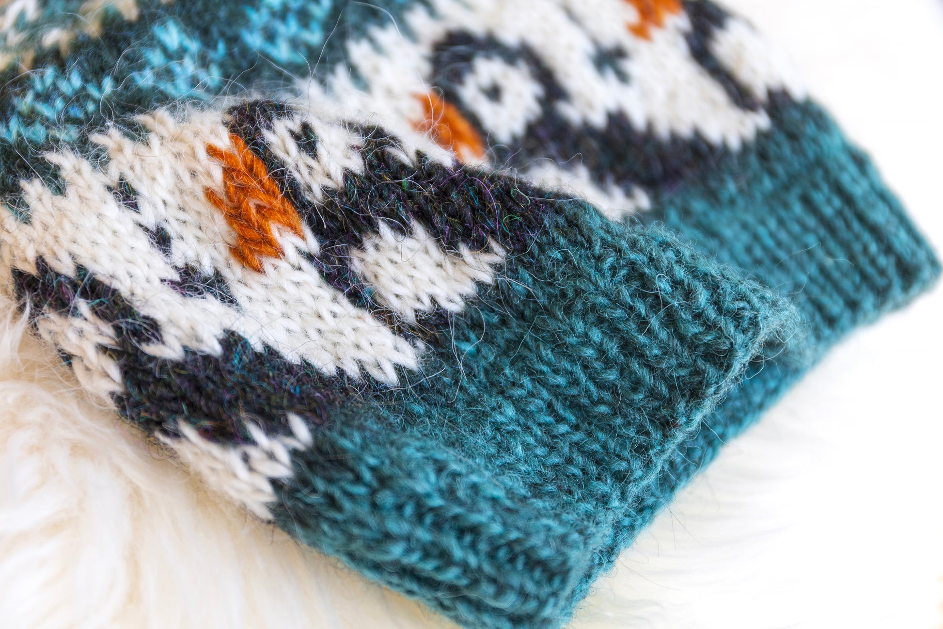 detail of a hand-knitted wool hat with a geometric pattern featuring puffins in blue, black, and brown colors on a white background.