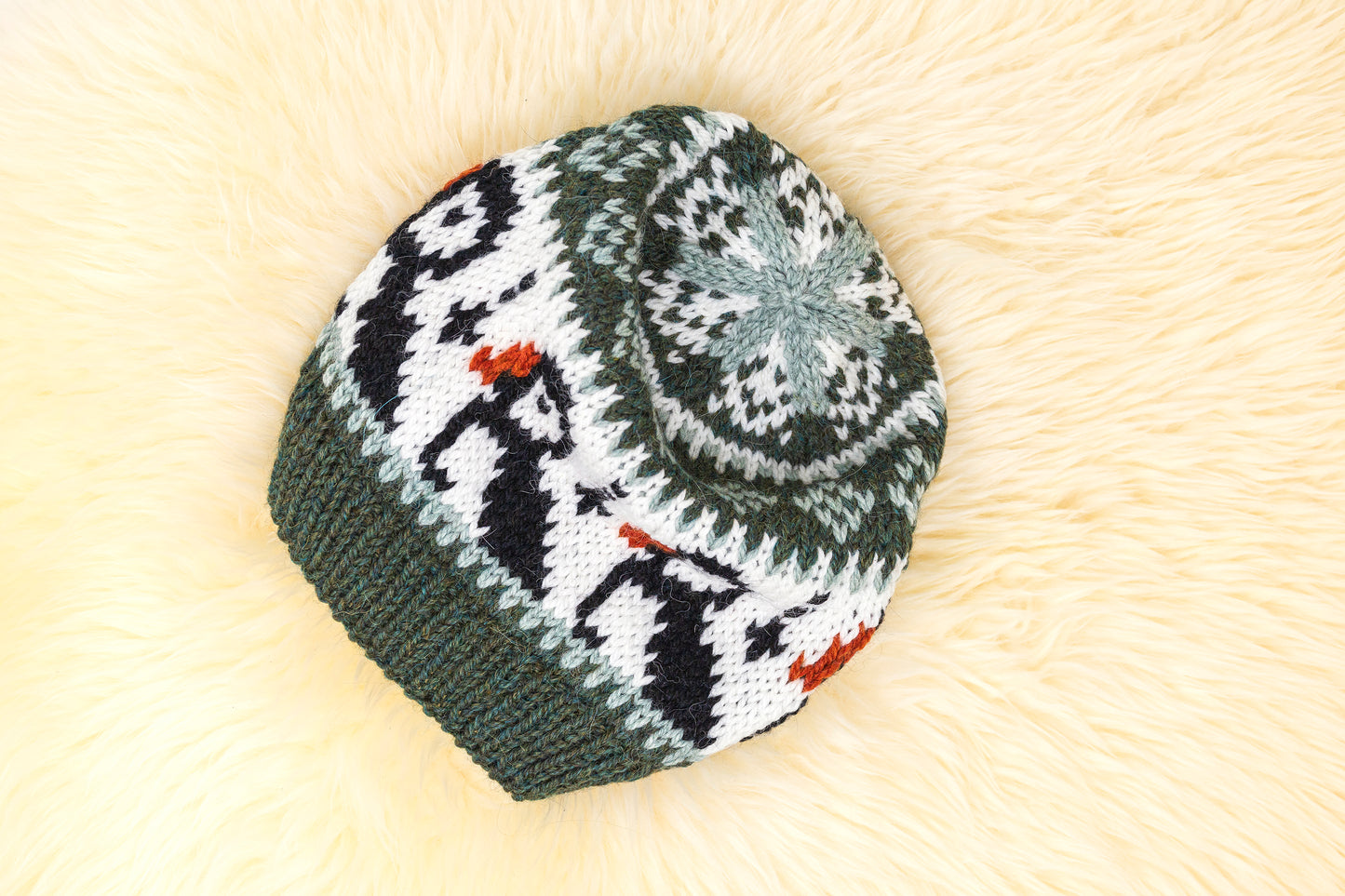 a hand-knitted wool hat with a geometric pattern featuring puffins in green, black and white colors on a white background.