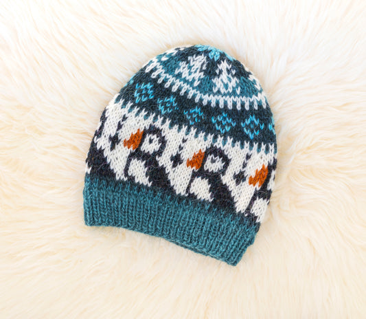 A hand-knitted wool hat with a geometric pattern featuring puffins in blue, black, and brown colors on a white background.