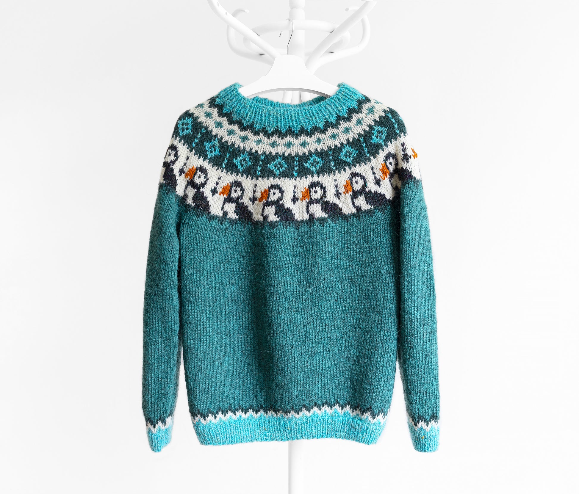 A teal Icelandic lopapeysa sweater with a colorful puffin Fair Isle yoke pattern, hanging on a white hanger against a white background.
