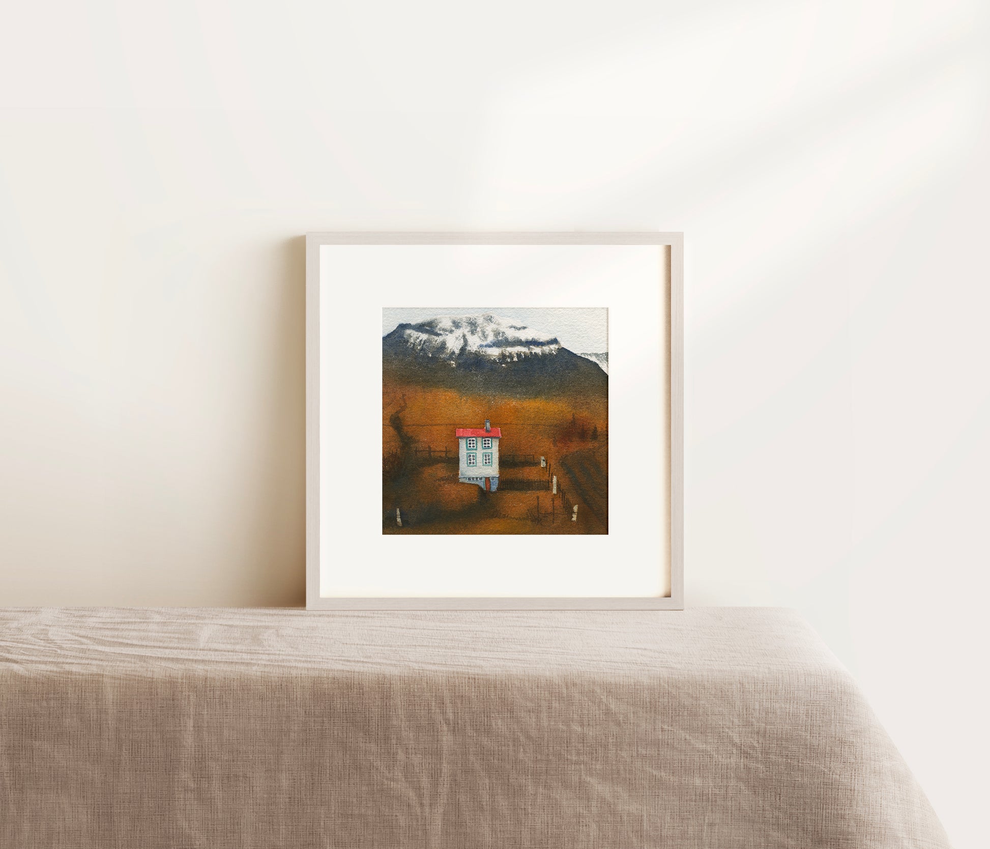 Framed artwork of a mountain landscape with a cabin on a white wall.