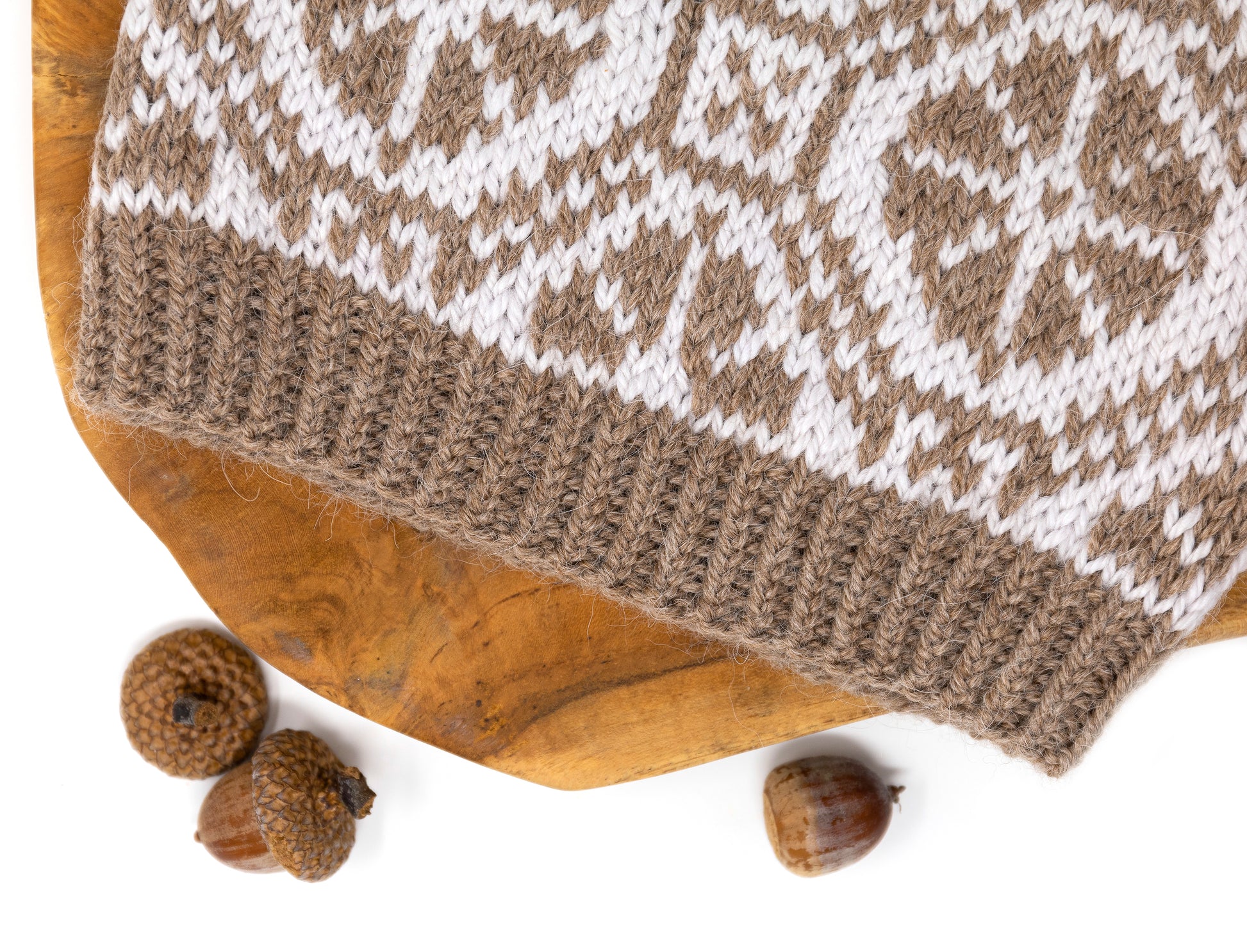Close-up for the twist ribbing of a hand-knitted Ratas Fair Isle hat with a wheel pattern on a wooden surface with acorns.