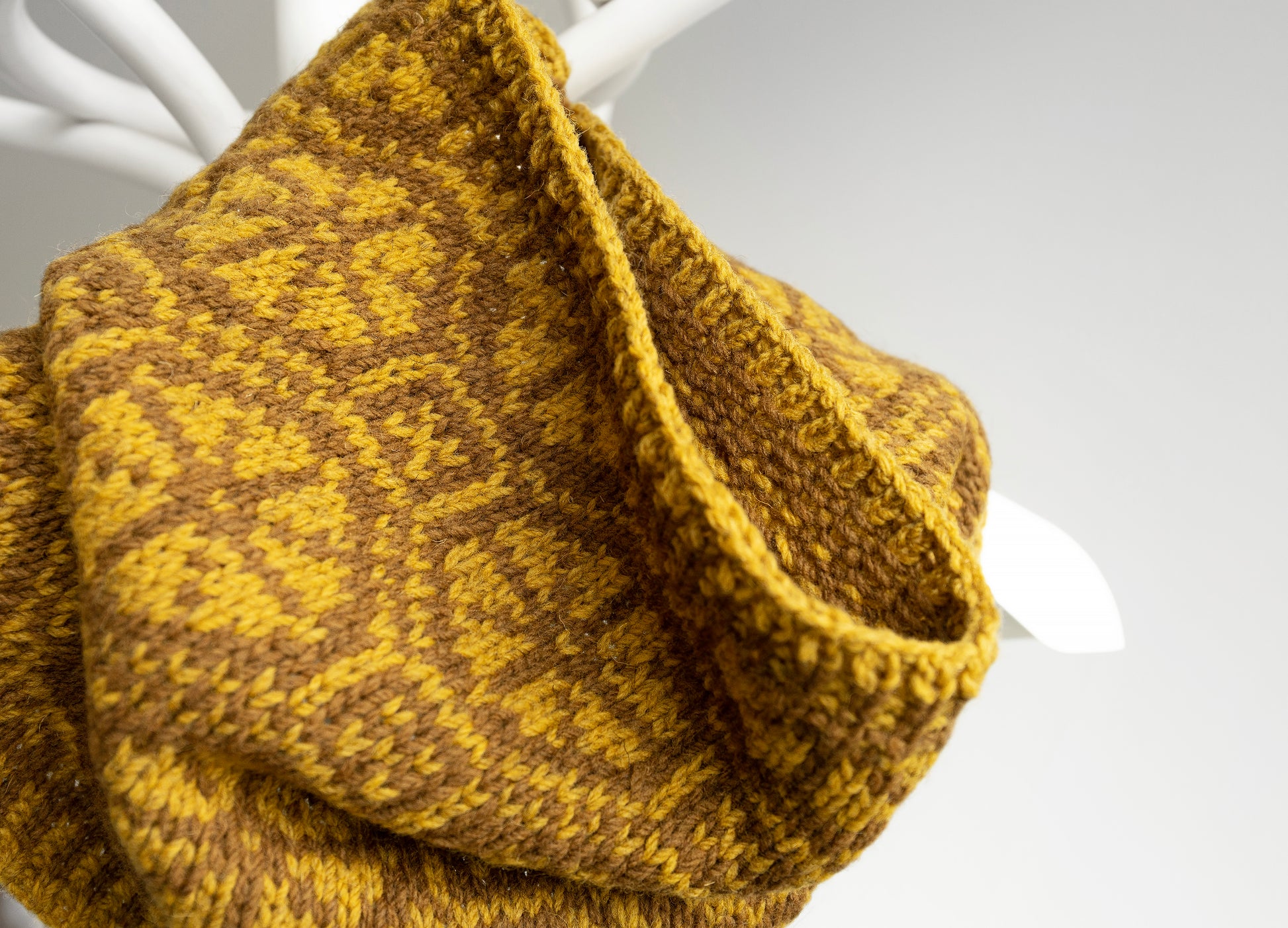 Hand-knitted mustard yellow cowl on a white stand against a light gray background