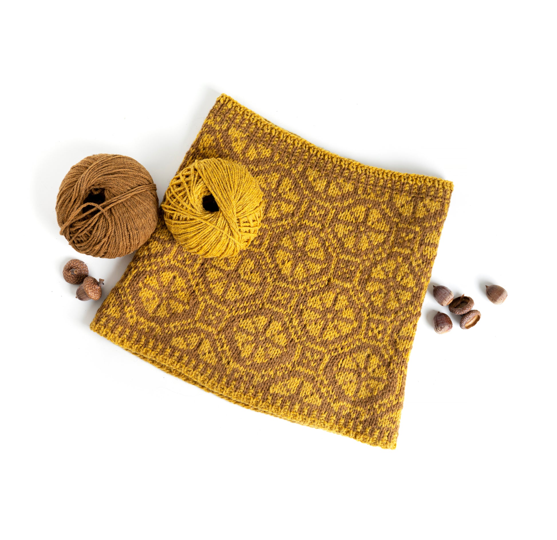 hand-knitted Ratas cowl with a wheels pattern next to two balls of yarn on a white background