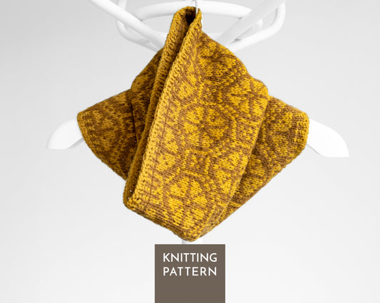 A hand-knitted Ratas cowl in mustard yellow and brown with a textured geometric pattern, displayed on a white hanger against a light gray background.