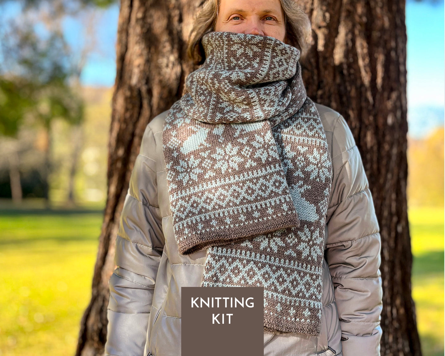 A man outdoors in front of a tree wearing a knitted scarf with a brown and off-white Fair Isle pattern, with a 'KNITTING KIT' label overlay at the bottom.