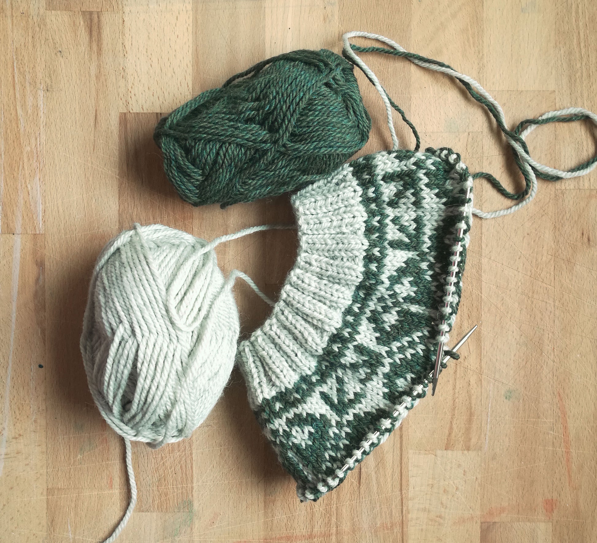 beige and green wool hand-knitted Fair Isle beanie hat in snowflake knitting pattern in progress with needles and yarn balls