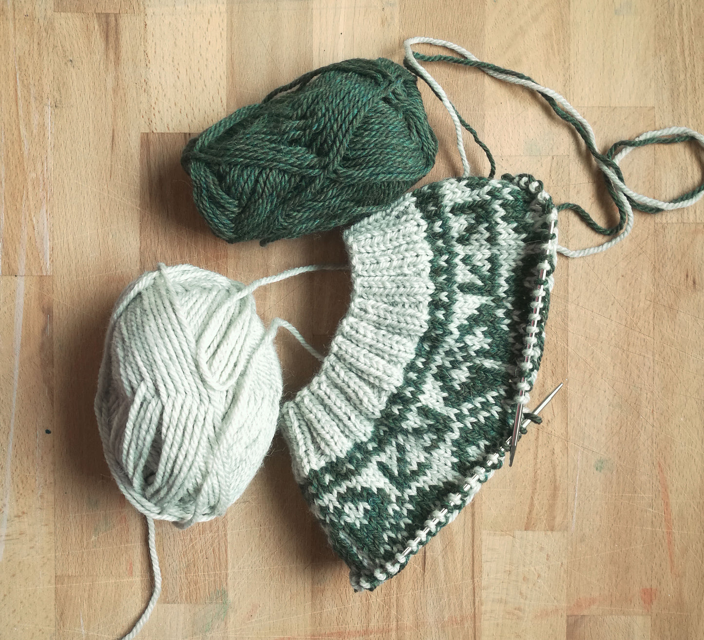 beige and green wool hand-knitted Fair Isle beanie hat in snowflake knitting pattern in progress with needles and yarn balls