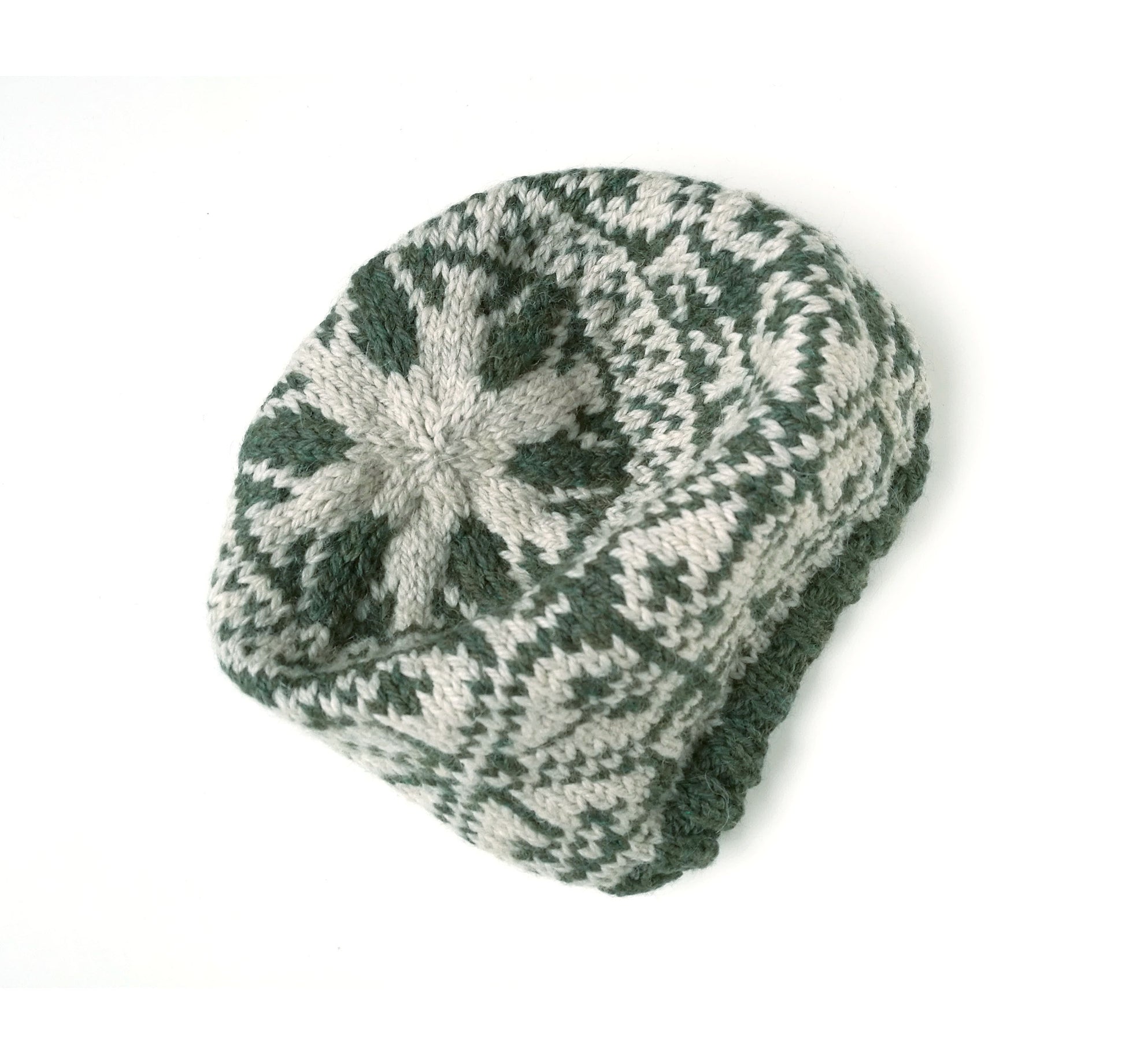 A hand-knit slouchy beanie hat featuring a dark green and light gray snowflake pattern, photographed on a clean white background.