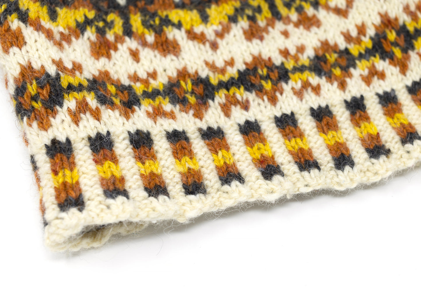 Close-up of a knitted Fair Isle beanie hat with a cream base and horizontal rows of brown, black, and yellow geometric patterns.