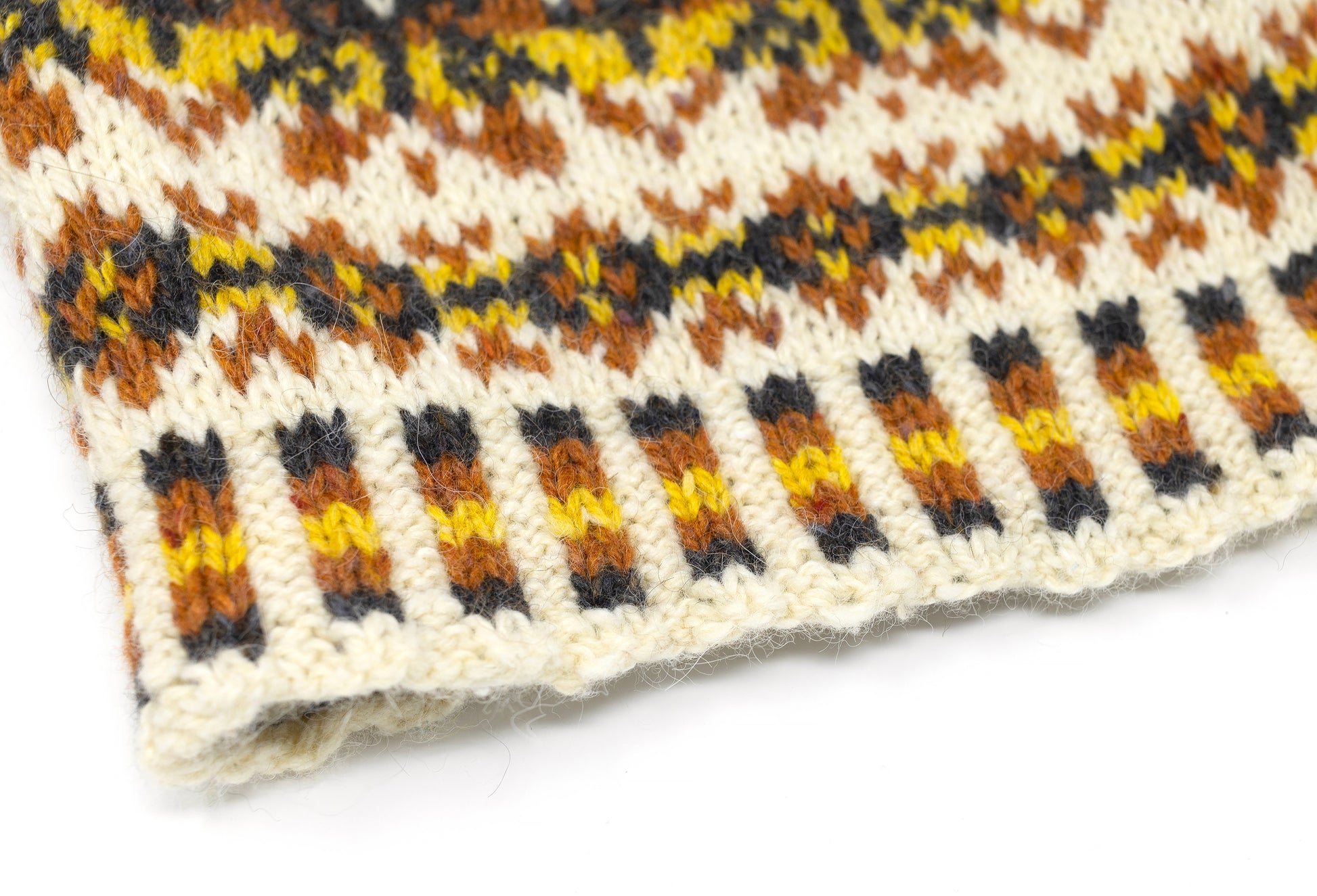 Close-up of a knitted Fair Isle beanie hat with a cream base and horizontal rows of brown, black, and yellow geometric patterns.