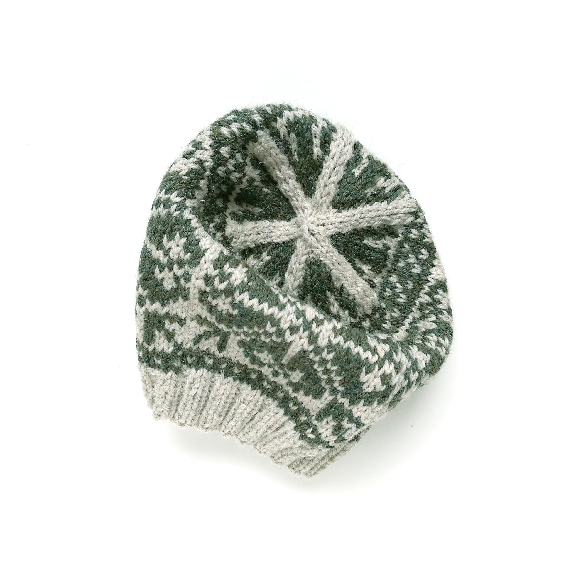 A crown of a beige and green wool hand-knitted Fair Isle beanie hat with a snowflake motif