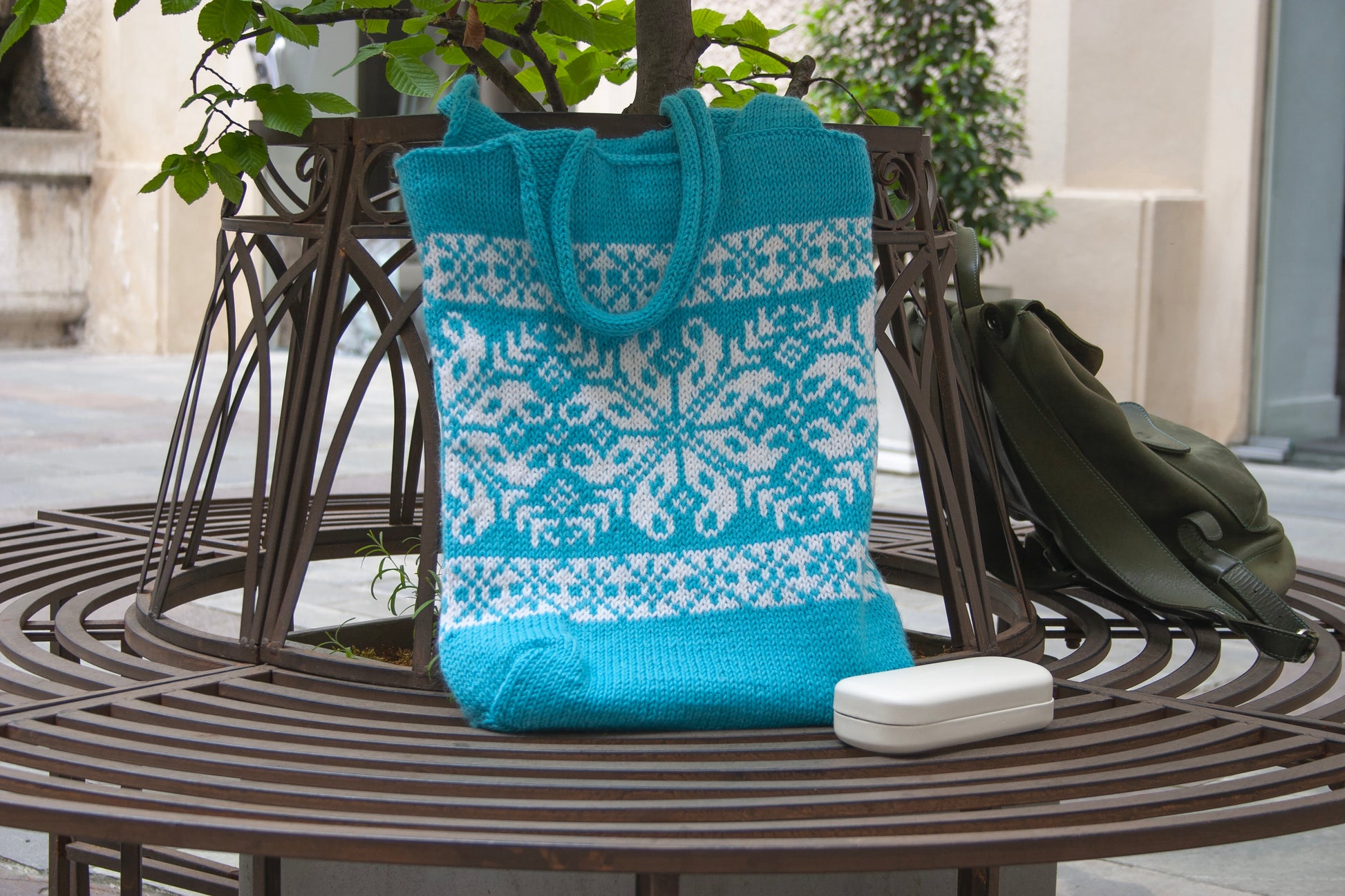 Turquoise and white Snowflake Selbu hand-knitted tote bag displayed in the urban exterior

