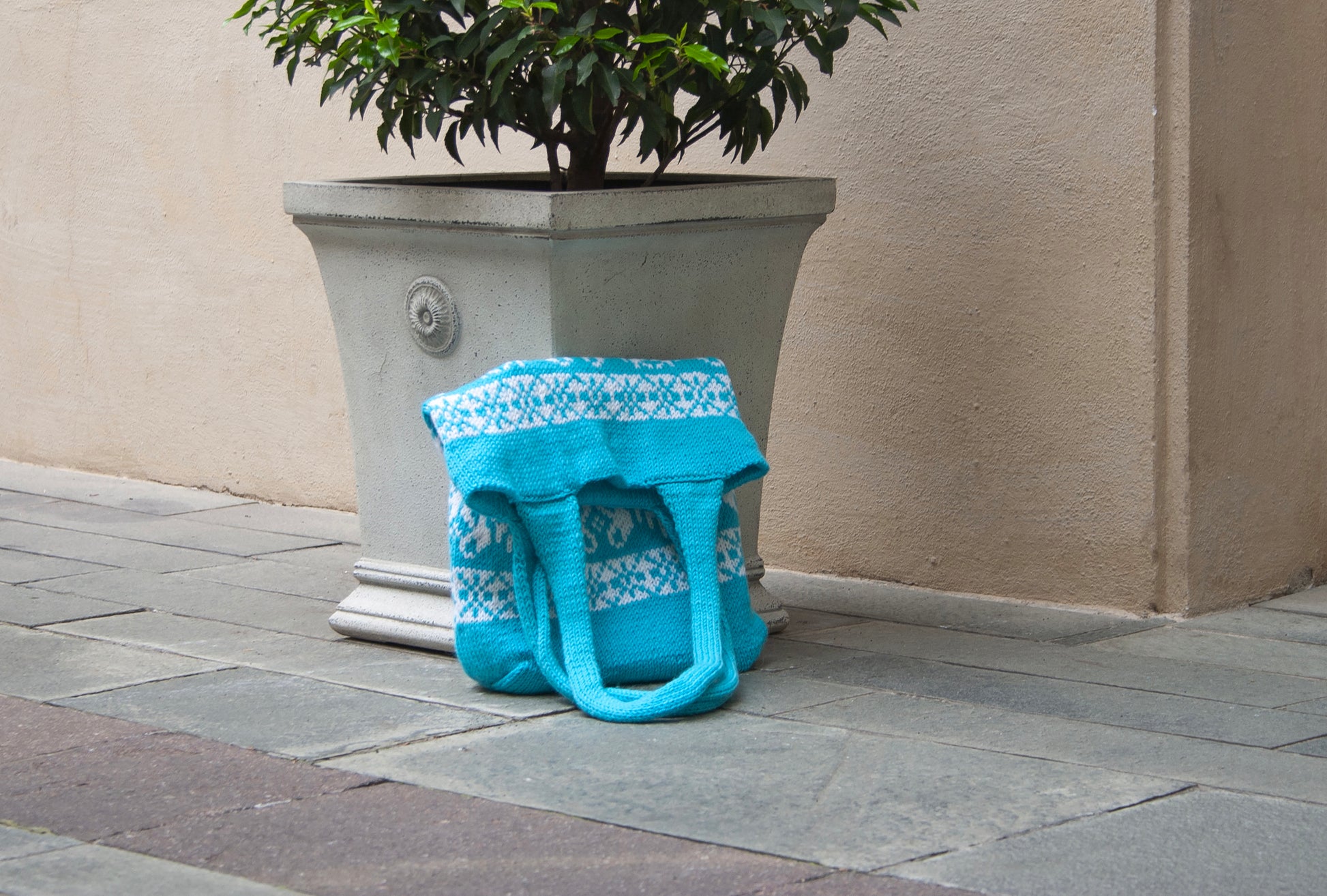 Turquoise and white Snowflake Selbu hand-knitted tote bag on a street