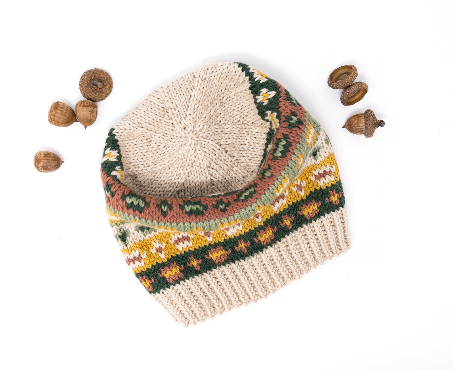 A crown of a hand-knitted hat with Fair Isle pattern, displayed on a white background with acorns