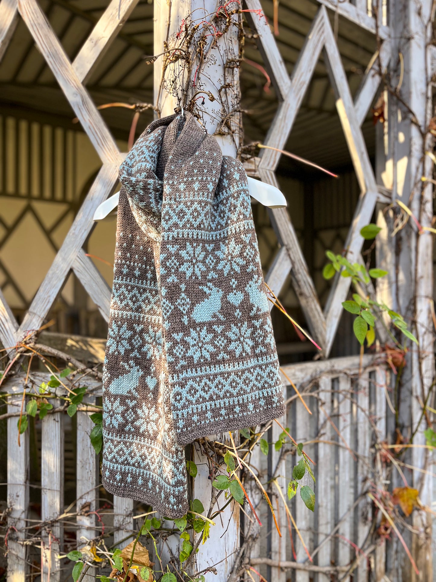 Sonka Bunny Fair Isle scarf hanging on a fence in a park