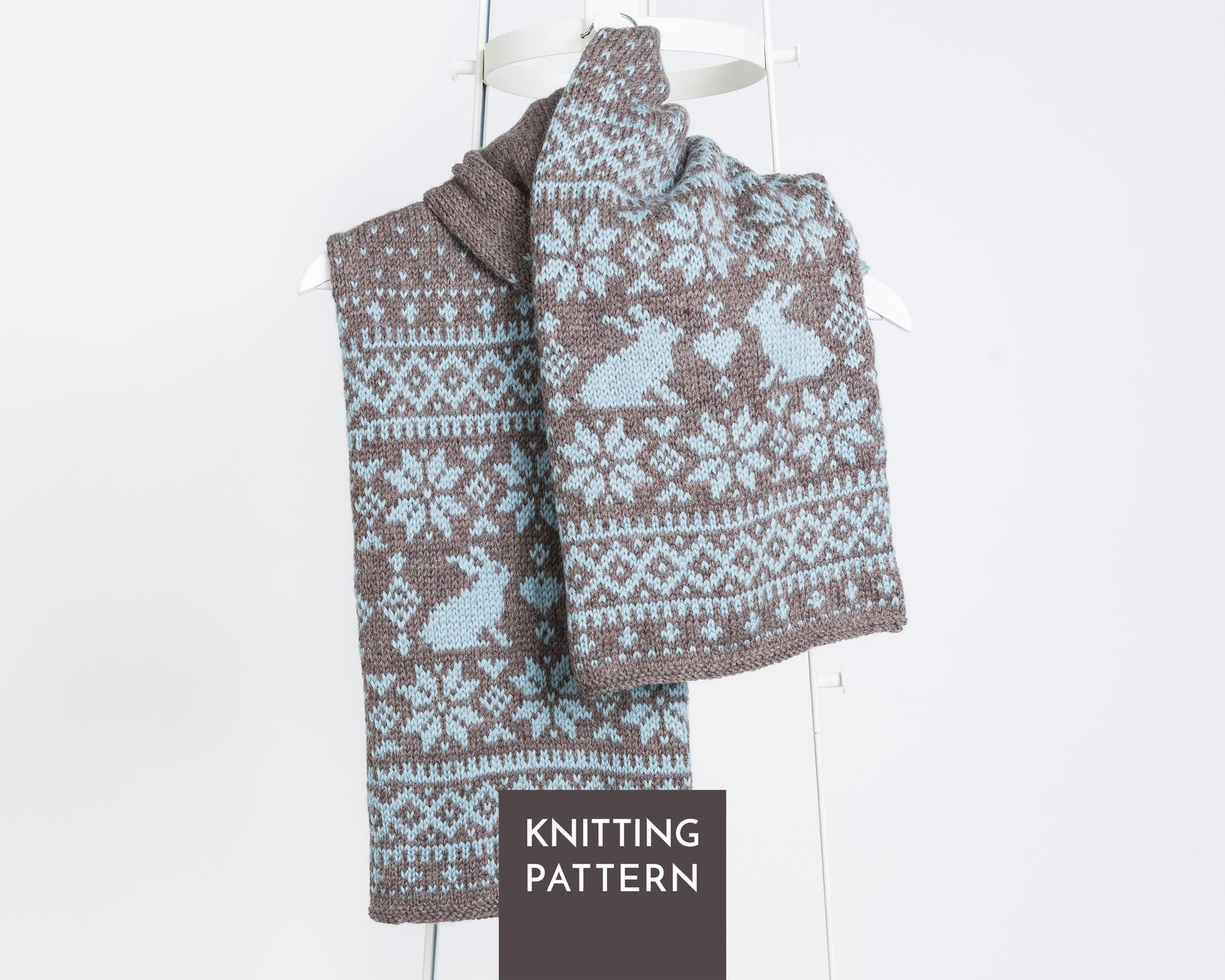 Sonka Bunny fair isle hand-knitted scarf with a brown and light blue Fair Isle pattern featuring rabbits and snowflakes, draped on a white hanger.