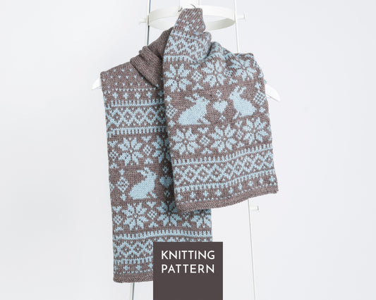 Sonka Bunny fair isle hand-knitted scarf with a brown and light blue Fair Isle pattern featuring rabbits and snowflakes, draped on a white hanger.