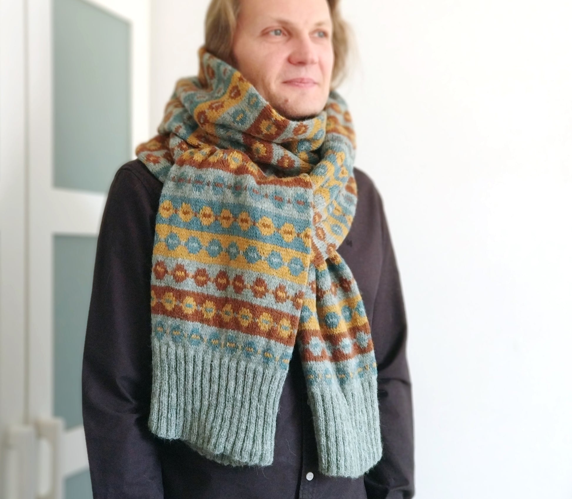 a man performs a long hand-knitted Fair Isle scarf made from grey blue, brown and yellow wool