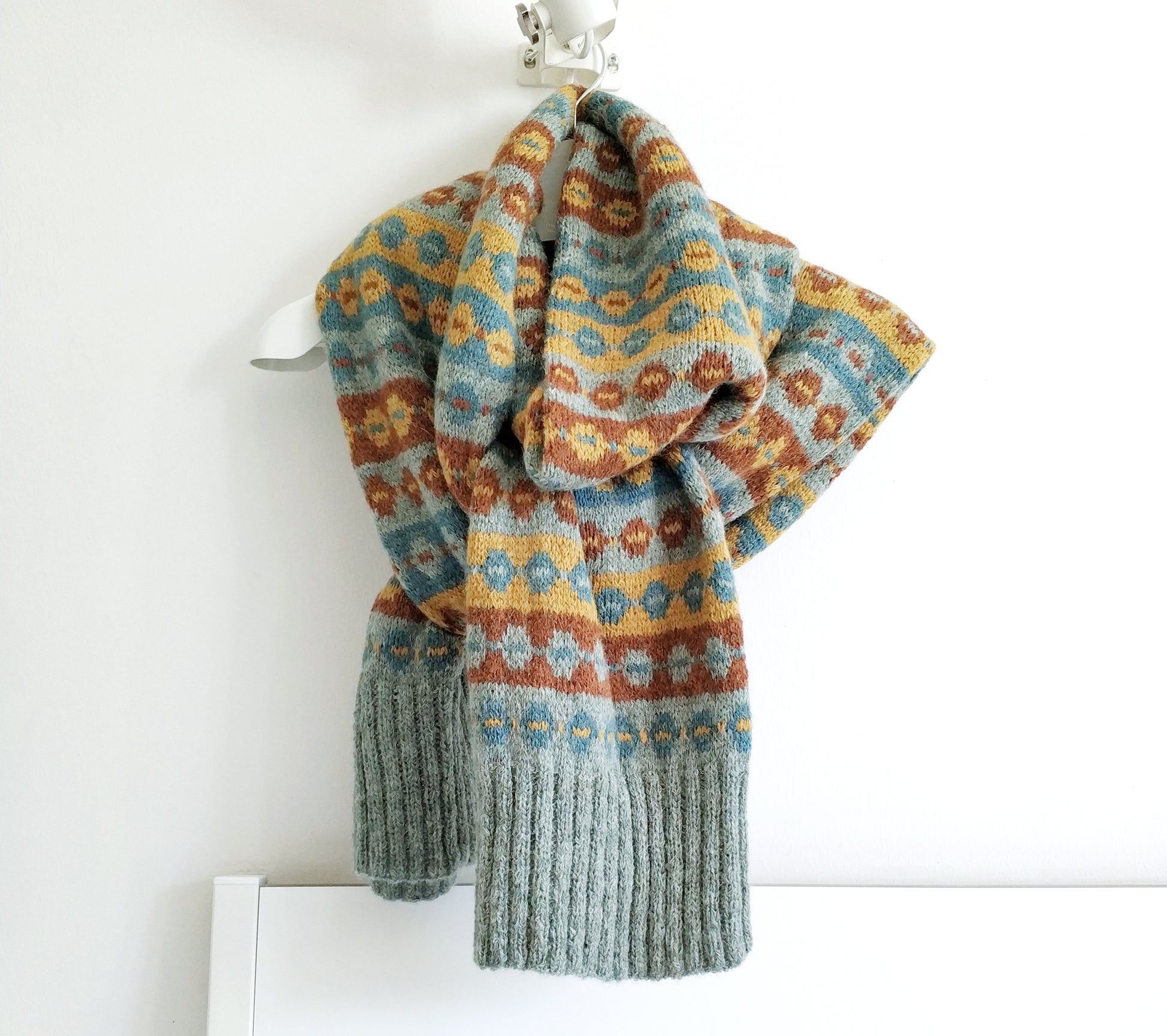 a long hand-knitted Fair Isle scarf made from grey blue, brown and yellow wool
