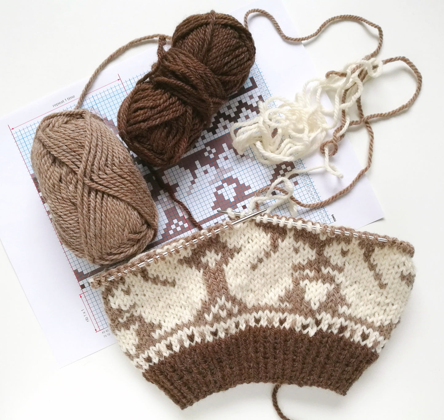 brown and white wool hand-knitted Fair Isle beanie hat with a squirrel motif in progress with yarn skeins and pattern booklet