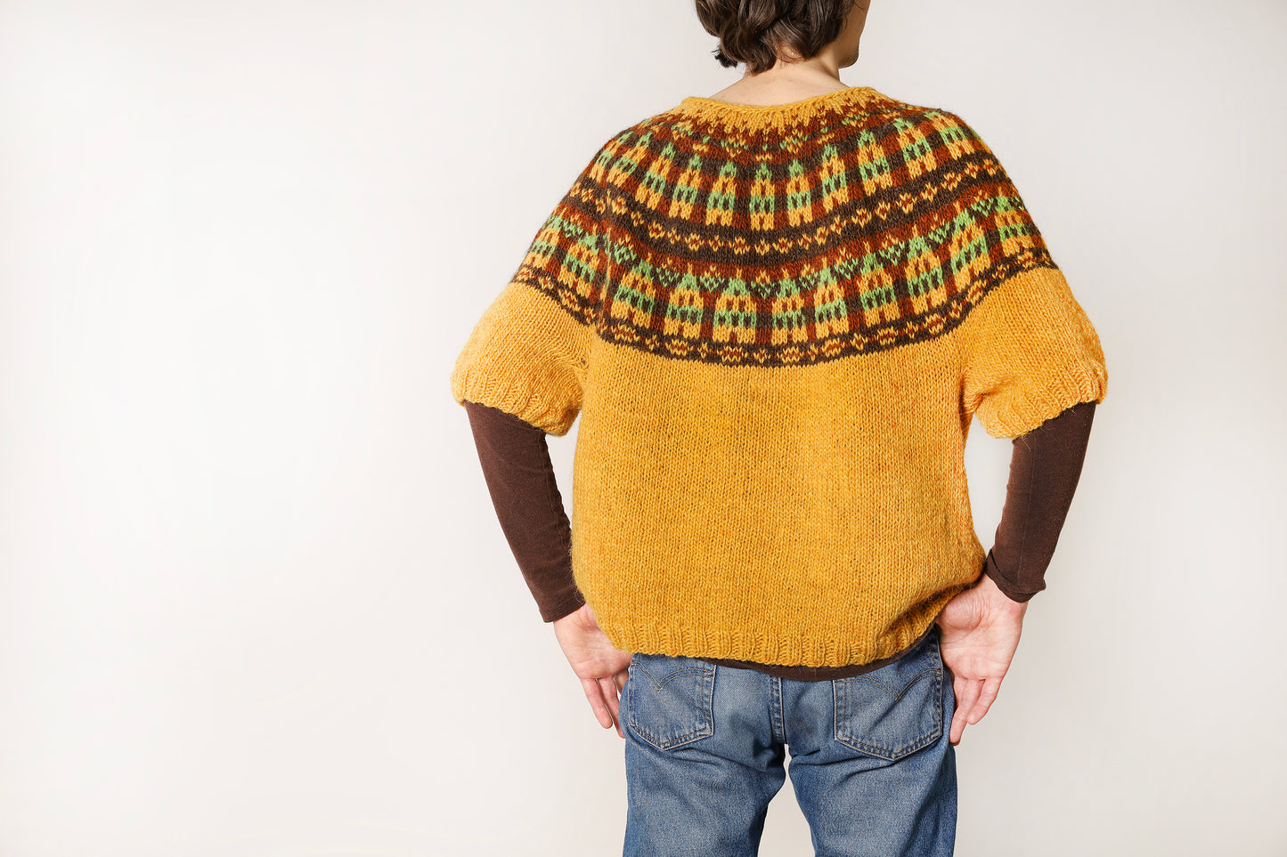 Back view of a person wearing a mustard yellow sweater with a patterned yoke with nordic houses