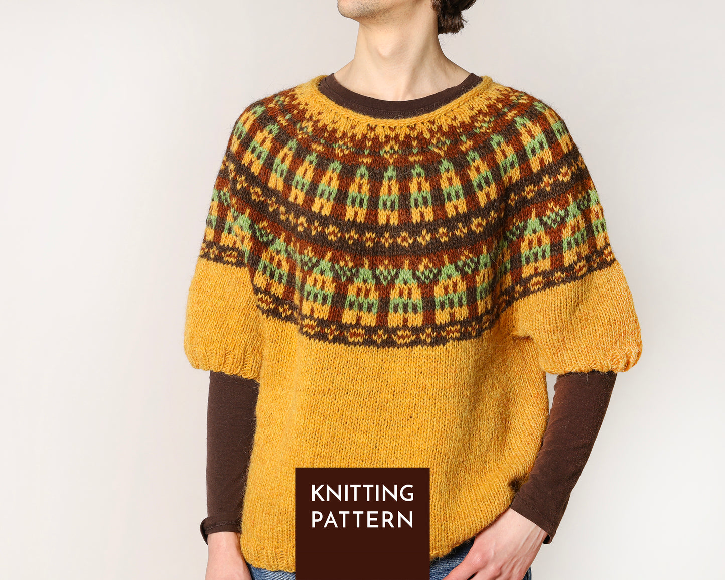 A person wearing a knitted sweater with a brown and mustard yellow colorwork yoke with nordic houses motif and solid mustard body.