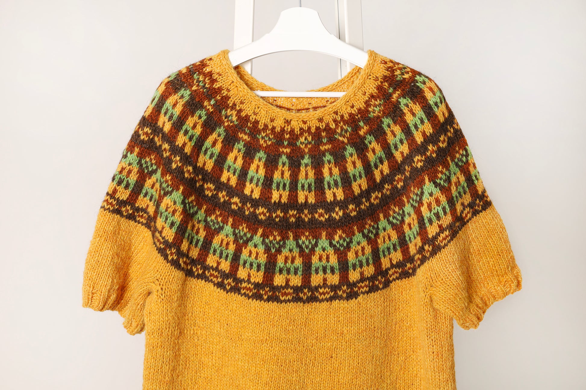 Stortorget icelandic lopapeysa sweater with a patterned yoke with nordic houses motif on a white hanger against a white background
