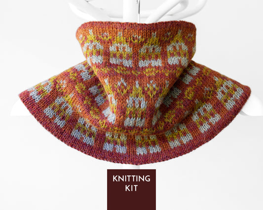 A knitted cowl or neck warmer with a wide brim, shown draped on a white mannequin stand. The knit pattern features a warm rust red base with yellow and white Fair Isle style motifs.