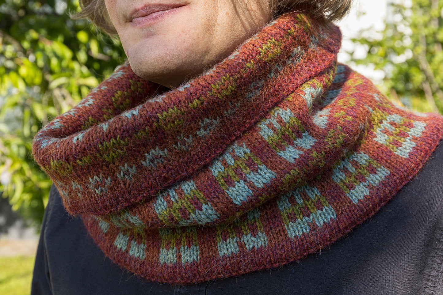 Person wearing a patterned knitted cowl with a blurred natural background