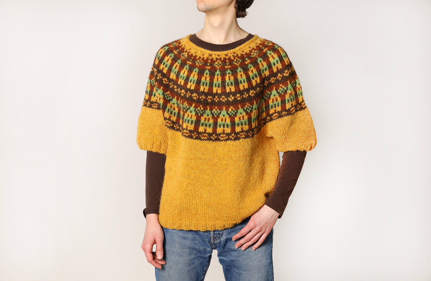 Person wearing a mustard yellow and brown patterned icelandic sweater on a white background
