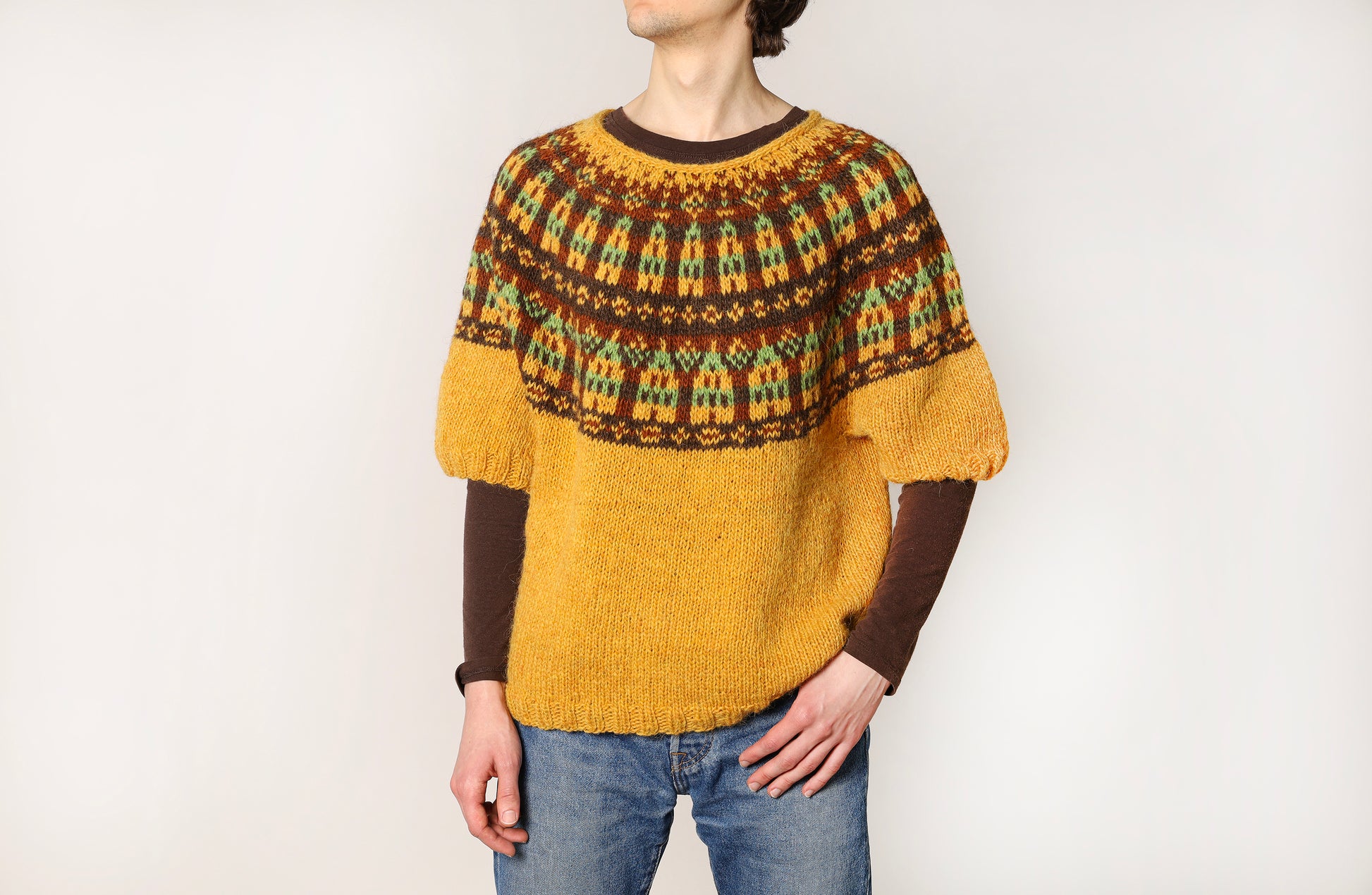 Person wearing a mustard yellow and brown patterned icelandic sweater on a white background
