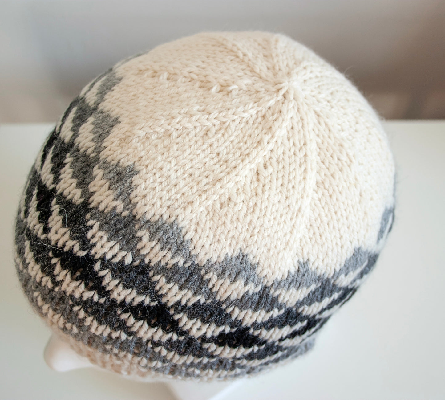 A crown of a white, grey and black wool hand-knitted Fair Isle beanie hat in triangles knitting pattern