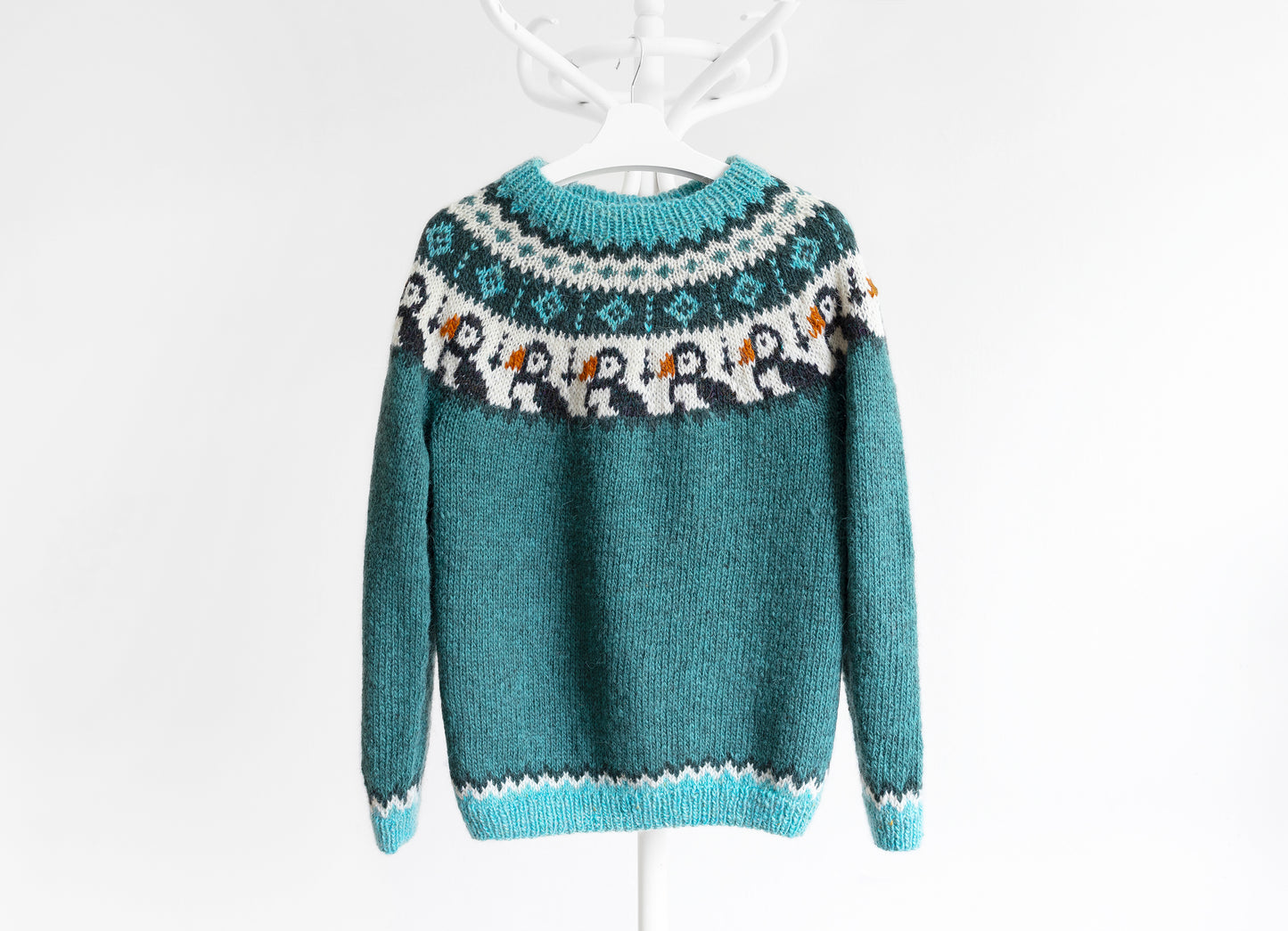 A knitted icelandic sweater with a geometric pattern featuring puffin motifs, predominantly in shades of blue and white.