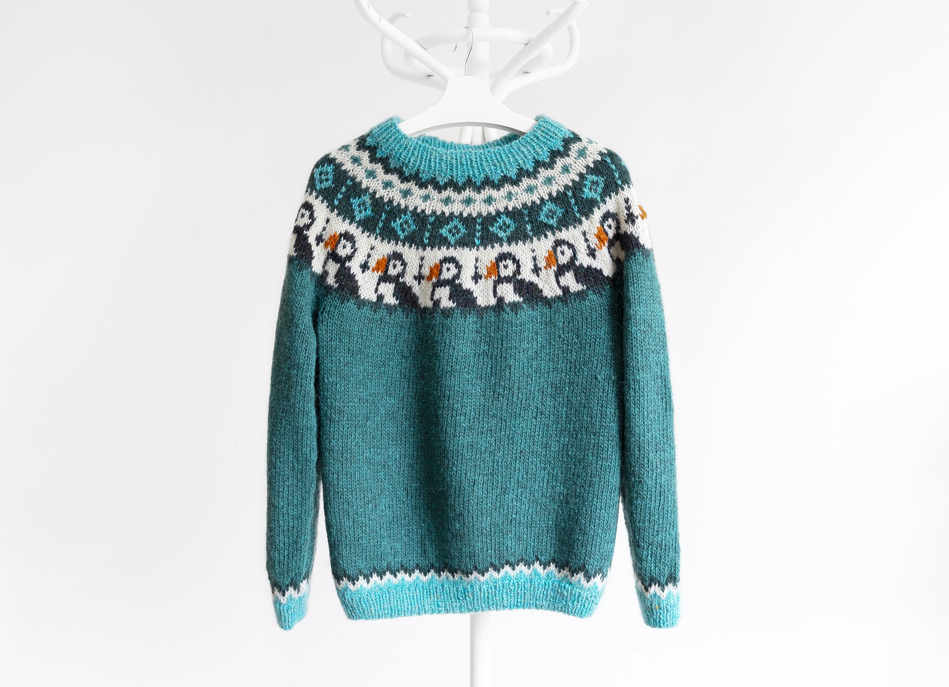 A knitted icelandic sweater with a geometric pattern featuring puffin motifs, predominantly in shades of blue and white.