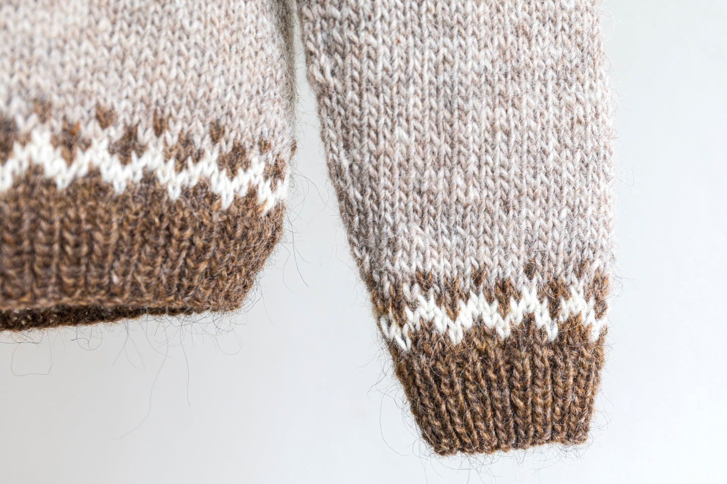 Details of a cuff and a hem of brown and white icelandic wool sweater