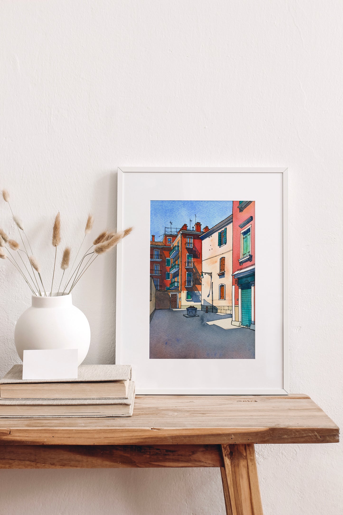 Framed watercolor artwork of a Venetian street scene on a wooden table with decorative elements.