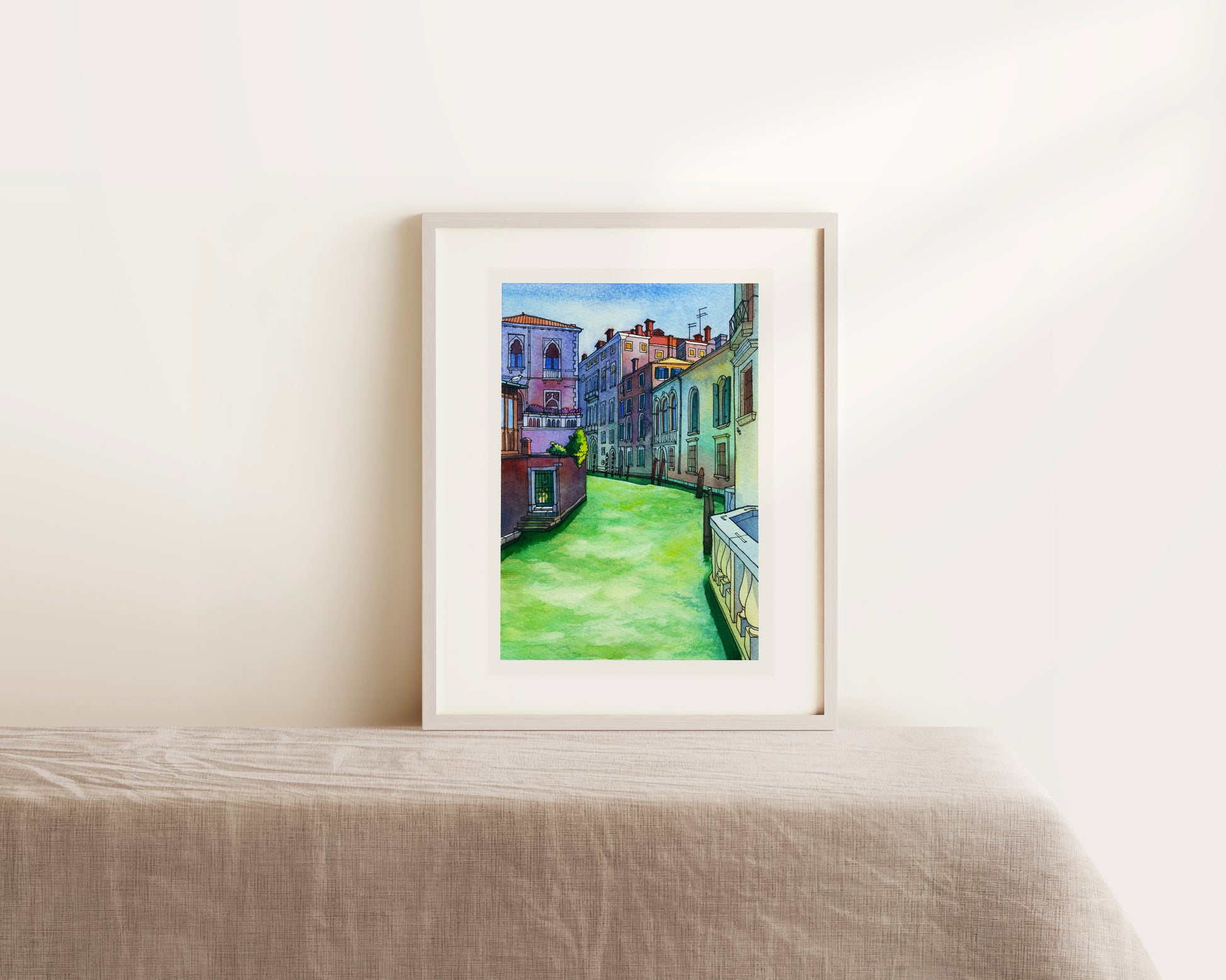 Framed watercolor artwork of a colorful Venetian canal scene on a white wall above a bed.