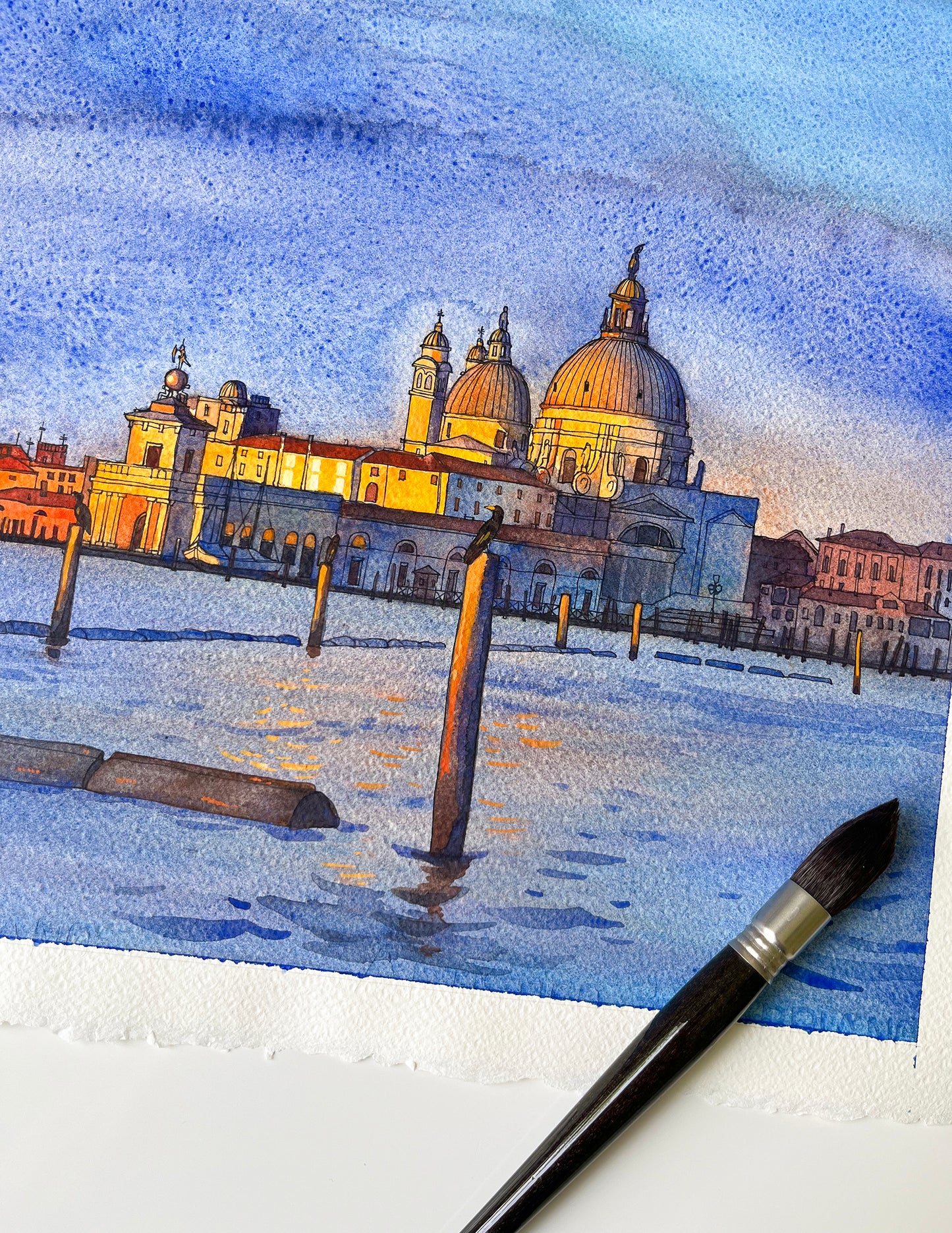 Watercolor painting of Venice San Marco basin at sunrise and a brush on a white surface