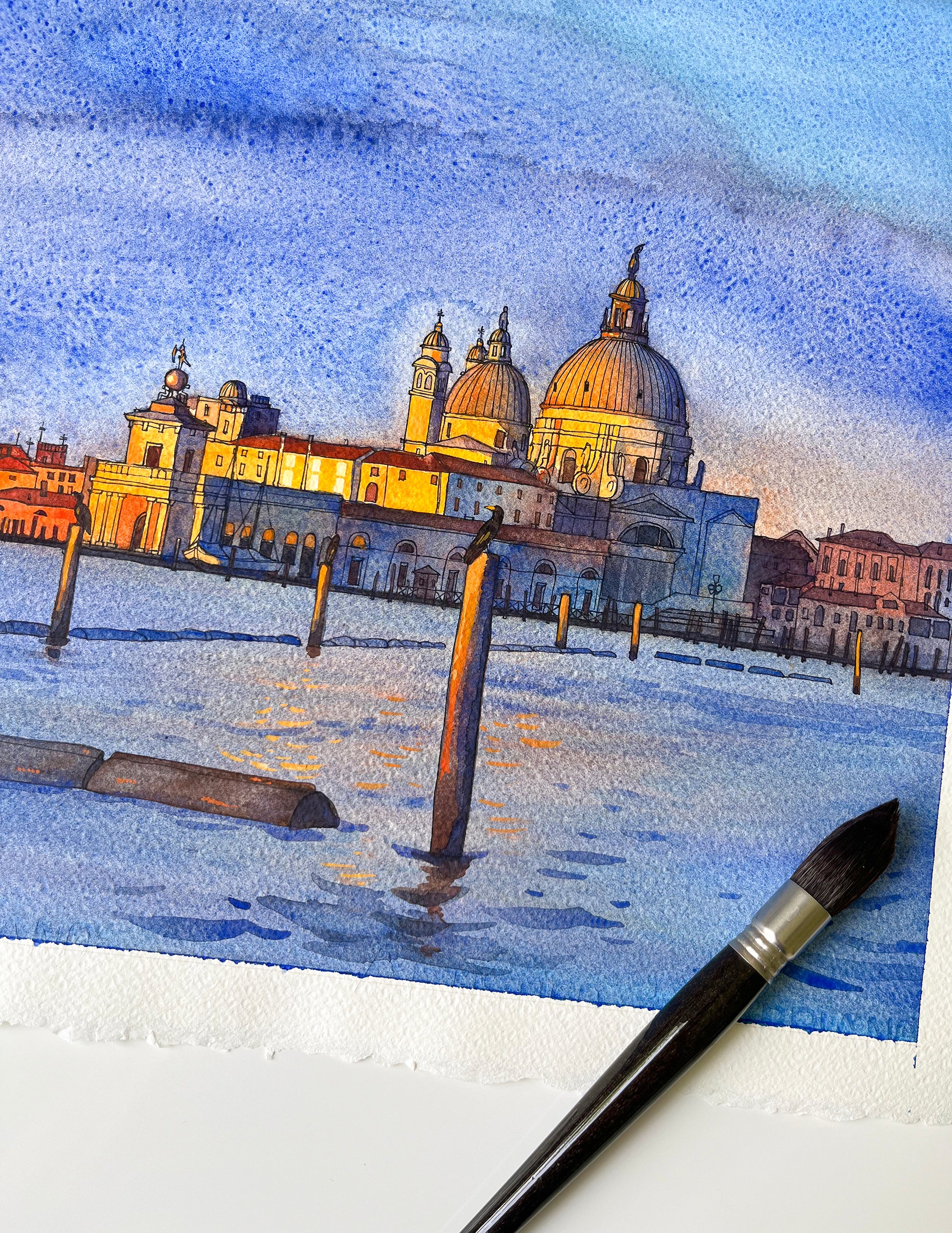 Watercolor painting of Venice San Marco basin at sunrise and a brush on a white surface