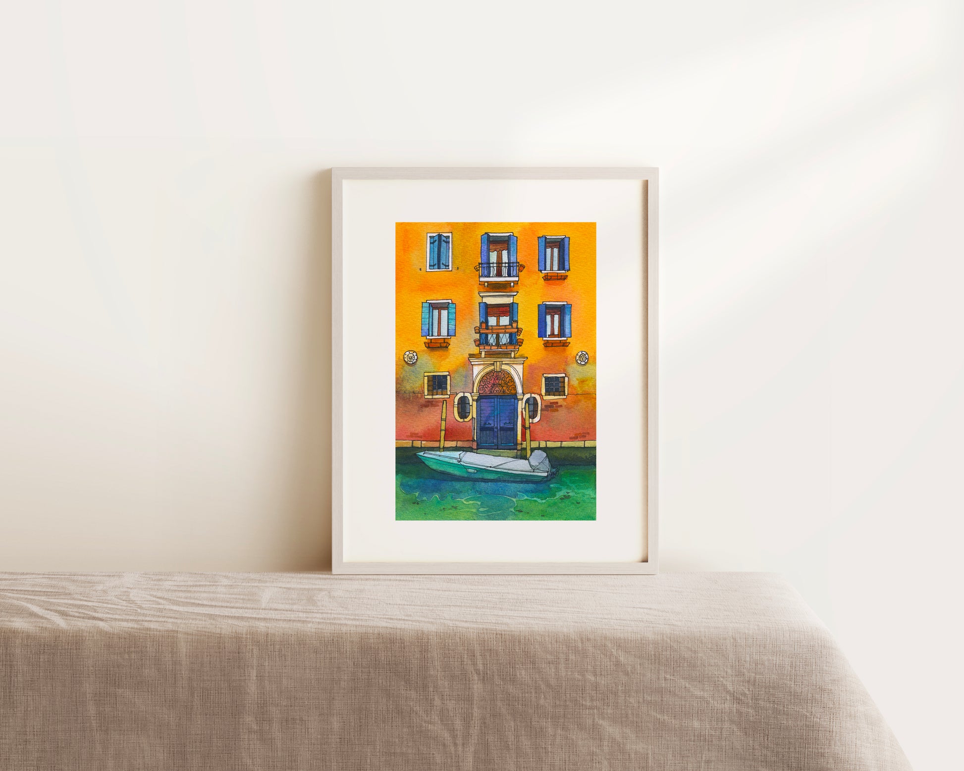 Framed watercolor artwork of a colorful Venetian building with a boat in front on a white surface.