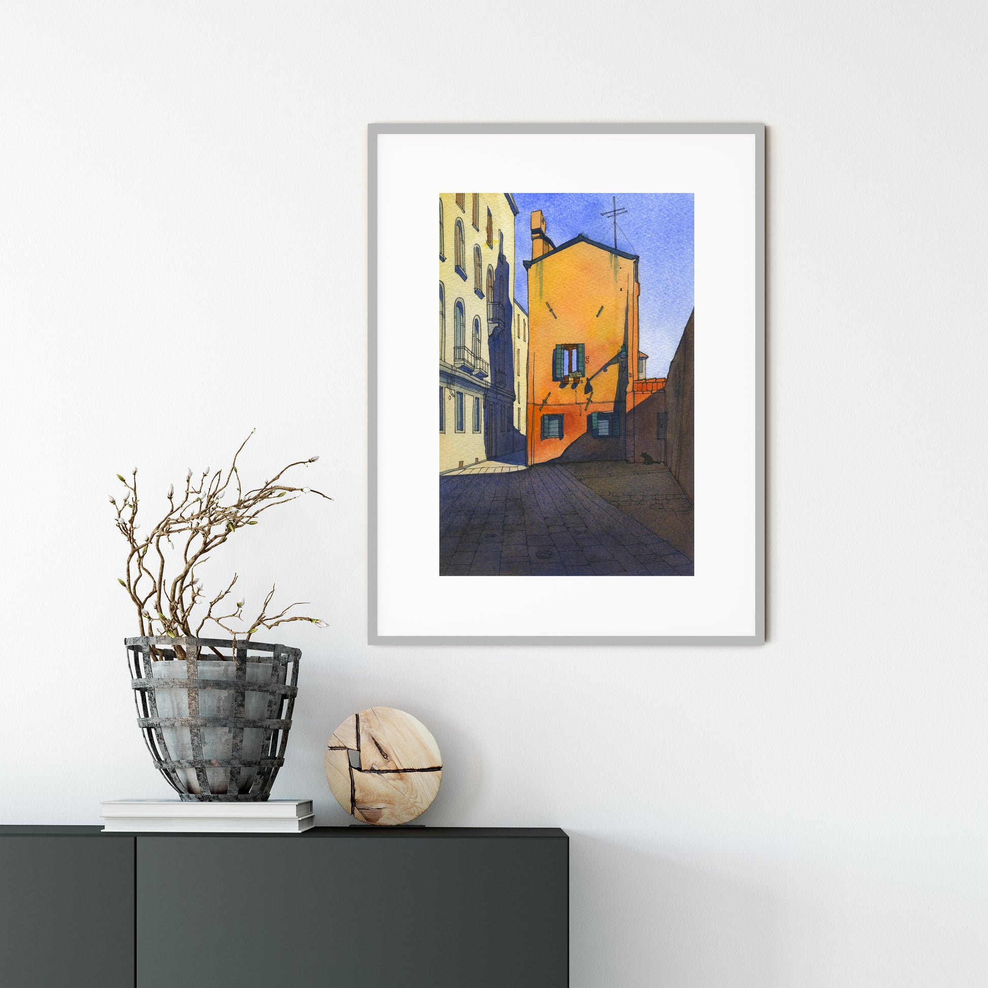 Framed watercolor and ink artwork of a city street scene in Cannaregio, Venice on a white wall with decorative items below.